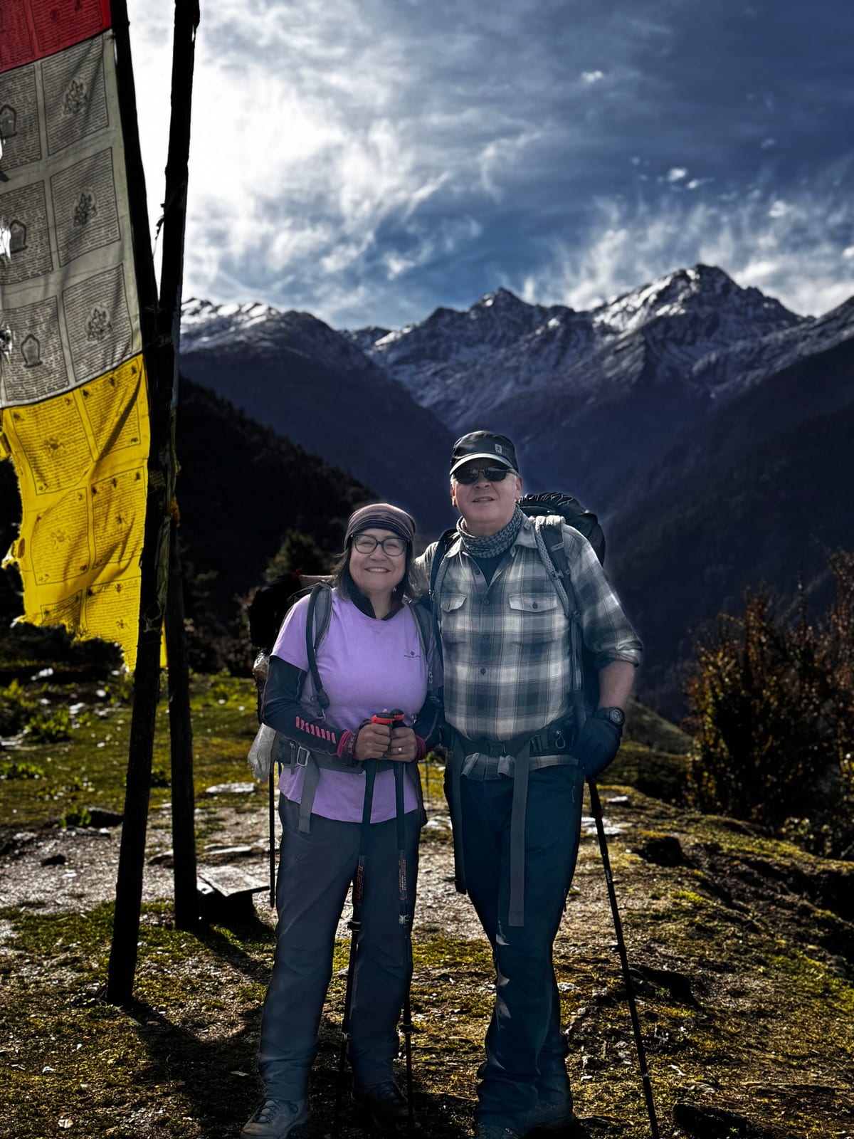 Two trekkers with poles beside a prayer-flag pole